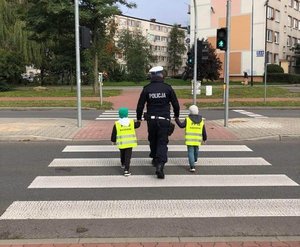 Policjant prowadzi dzieci przez przejście dla pieszych.