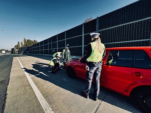 Czerwony samochód, policjanci i inspektorzy transportu drogowego sprawdzają światła.