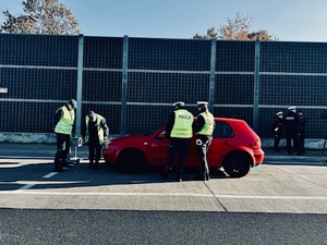 Czerwony samochód, policjanci i inspektorzy transportu drogowego sprawdzają światła.