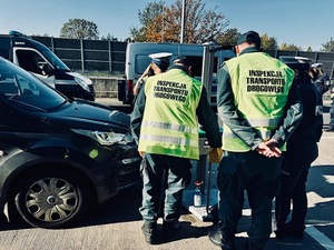 Czerwony samochód, policjanci i inspektorzy transportu drogowego sprawdzają światła.