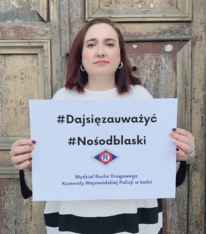 Kobieta trzyma w ręku kartkę z napisem #Daj się zauważyć#noś odblaski.