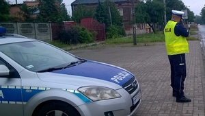 Policjant mierzy prędkość, obok radiowóz.