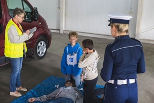 Policjantka z Ruchu Drogowego, dzieci wykonują zdanie z pierwszej pomocy.