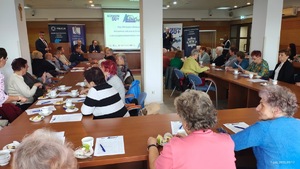 Policjanci prowadza profilaktykę wśród seniorów, seniorzy siedzą za stołami.