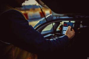 Policjant trzyma w ręku urządzenie do pomiaru poziomu alkoholu we krwi.