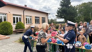 Policjantka przekazuje pani dyrektor kask z tyłu dzieci i kaski.