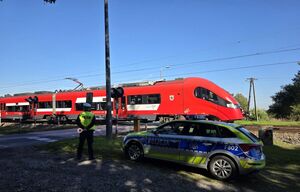 Policjant, radiowóz i przejeżdżający pociąg.
