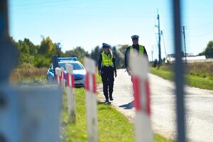 Policjanci idą od radiowozu do przejazdu kolejowego.