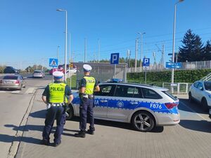 Policjanci przy radiowozie obserwujący przejeżdżające samochody.