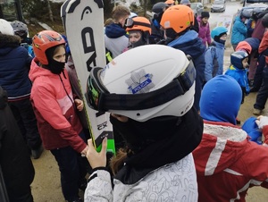 Na zdjęciu widać grupę dzieci, na głowach mają założone kaski ochronne, w rękach trzymają narty.
