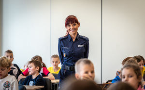 Policjantka wśród dzieci siedzących w ławce.