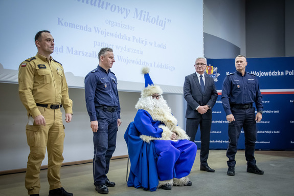 Niebieski mikołaj siedzi na krześle obok kierownictwo KWP w Łodzi i straży pożarnej.