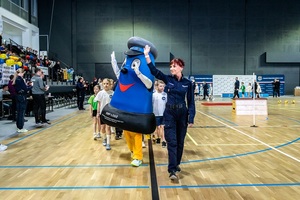 Zmagania dzieci podczas zawodów sportowych na sali gimnastycznej w obecności policjantów i aktorów.