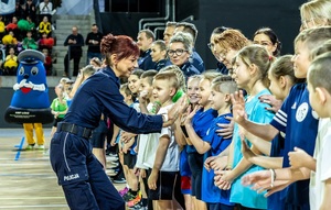 Zmagania dzieci podczas zawodów sportowych na sali gimnastycznej w obecności policjantów i aktorów.