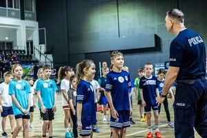 Zmagania dzieci podczas zawodów sportowych na sali gimnastycznej w obecności policjantów i aktorów.