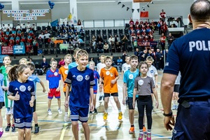 Zmagania dzieci podczas zawodów sportowych na sali gimnastycznej w obecności policjantów i aktorów.