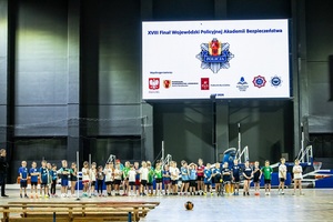 Zmagania dzieci podczas zawodów sportowych na sali gimnastycznej w obecności policjantów i aktorów.