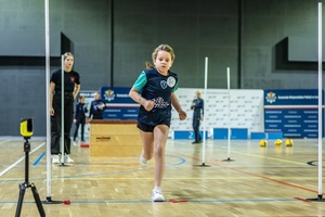 Zmagania dzieci podczas zawodów sportowych na sali gimnastycznej w obecności policjantów i aktorów.