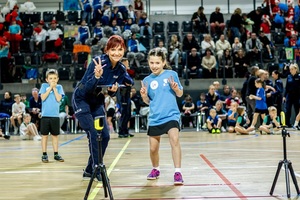 Zmagania dzieci podczas zawodów sportowych na sali gimnastycznej w obecności policjantów i aktorów.