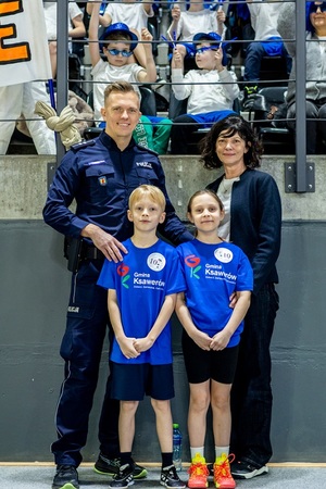 Zmagania dzieci podczas zawodów sportowych na sali gimnastycznej w obecności policjantów i aktorów.