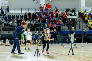 Zmagania dzieci podczas zawodów sportowych na sali gimnastycznej w obecności policjantów i aktorów.