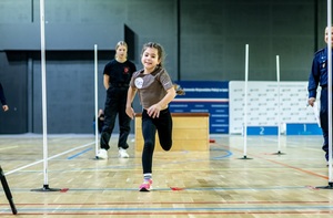 Zmagania sportowe dzieci na sali gimnastycznej w obecności policjantów  i aktorów.