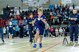 Zmagania sportowe dzieci na sali gimnastycznej w obecności policjantów  i aktorów.
