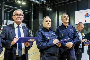 Zmagania sportowe dzieci na sali gimnastycznej w obecności policjantów  i aktorów.