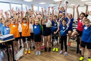 Zmagania dzieci podczas zawodów sportowych na sali gimnastycznej w obecności policjantów i aktorów.