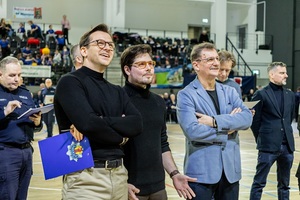 Zmagania dzieci podczas zawodów sportowych na sali gimnastycznej w obecności policjantów i aktorów.