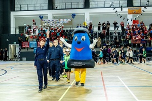 Zmagania dzieci podczas zawodów sportowych na sali gimnastycznej w obecności policjantów i aktorów.