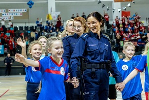 Zmagania dzieci podczas zawodów sportowych na sali gimnastycznej w obecności policjantów i aktorów.