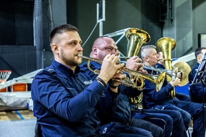 Zmagania dzieci podczas zawodów sportowych na sali gimnastycznej w obecności policjantów i aktorów.