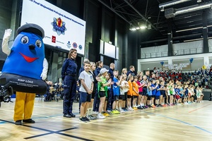 Zmagania dzieci podczas zawodów sportowych na sali gimnastycznej w obecności policjantów i aktorów.