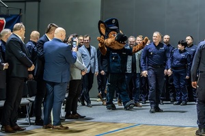 Zmagania dzieci podczas zawodów sportowych na sali gimnastycznej w obecności policjantów i aktorów.