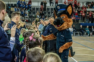 Zmagania dzieci podczas zawodów sportowych na sali gimnastycznej w obecności policjantów i aktorów.