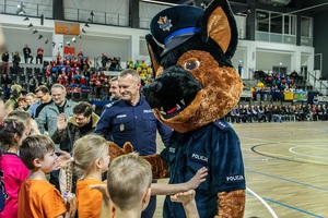 Zmagania dzieci podczas zawodów sportowych na sali gimnastycznej w obecności policjantów i aktorów.