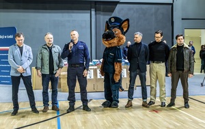 Zmagania dzieci podczas zawodów sportowych na sali gimnastycznej w obecności policjantów i aktorów.