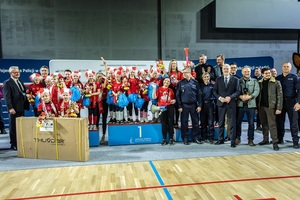 Zmagania dzieci podczas zawodów sportowych na sali gimnastycznej w obecności policjantów i aktorów.