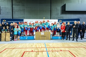 Zmagania dzieci podczas zawodów sportowych na sali gimnastycznej w obecności policjantów i aktorów.