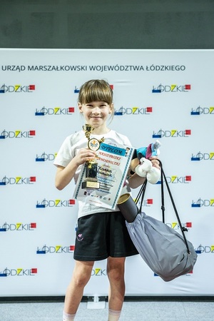 Zmagania dzieci podczas zawodów sportowych na sali gimnastycznej w obecności policjantów i aktorów.