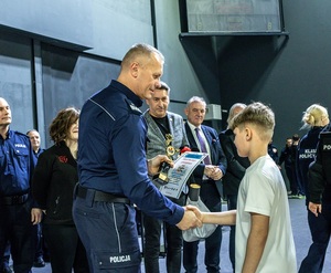 Zmagania dzieci podczas zawodów sportowych na sali gimnastycznej w obecności policjantów i aktorów.