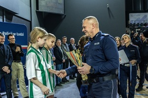 Zmagania dzieci podczas zawodów sportowych na sali gimnastycznej w obecności policjantów i aktorów.
