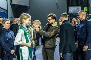 Zmagania dzieci podczas zawodów sportowych na sali gimnastycznej w obecności policjantów i aktorów.