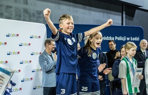 Zmagania dzieci podczas zawodów sportowych na sali gimnastycznej w obecności policjantów i aktorów.