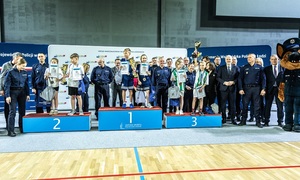 Zmagania dzieci podczas zawodów sportowych na sali gimnastycznej w obecności policjantów i aktorów.