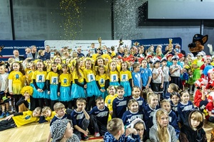 Zmagania dzieci podczas zawodów sportowych na sali gimnastycznej w obecności policjantów i aktorów.