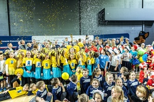 Zmagania dzieci podczas zawodów sportowych na sali gimnastycznej w obecności policjantów i aktorów.