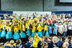 Zmagania dzieci podczas zawodów sportowych na sali gimnastycznej w obecności policjantów i aktorów.