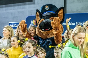 Zmagania dzieci podczas zawodów sportowych na sali gimnastycznej w obecności policjantów i aktorów.